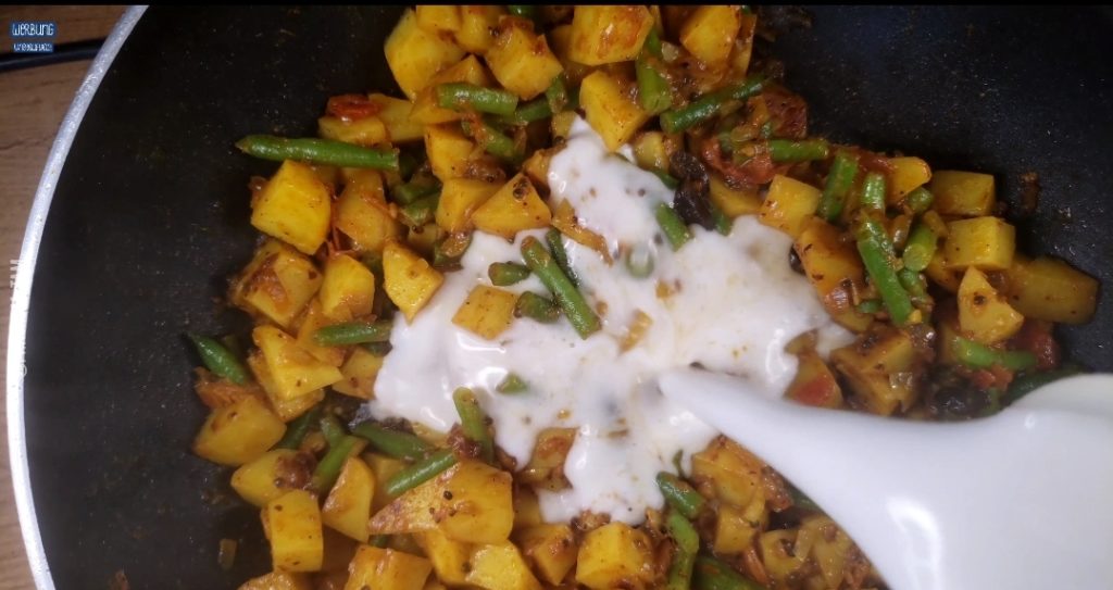 Indisches Kartoffel-Curry: Kokosmilch zu Kartoffeln angießen.